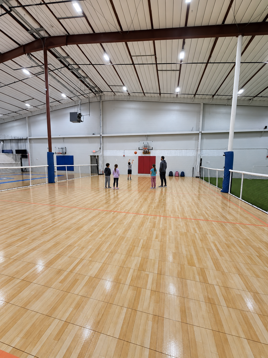 Children practicing basketball on the indoor wood hard court with a coach during an after-school program at PSA Sports Club