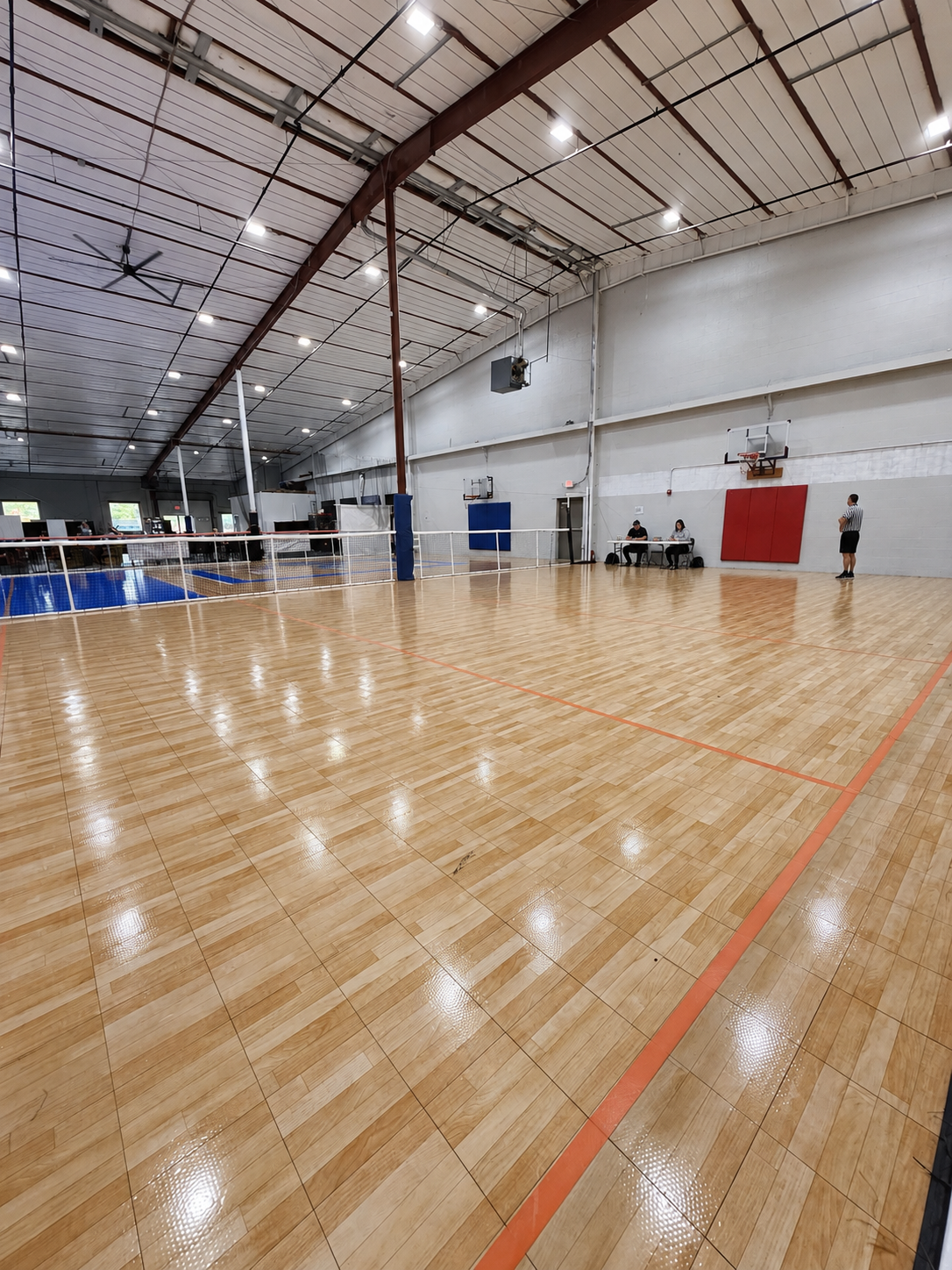 Indoor wood hard court with basketball hoops, blue wall padding and perimeter netting, set up for league and tournament play