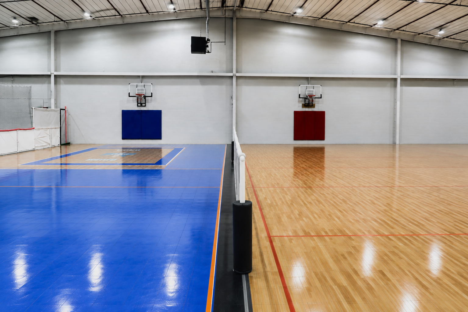 Indoor hard court set up with basketball hoops and a volleyball net