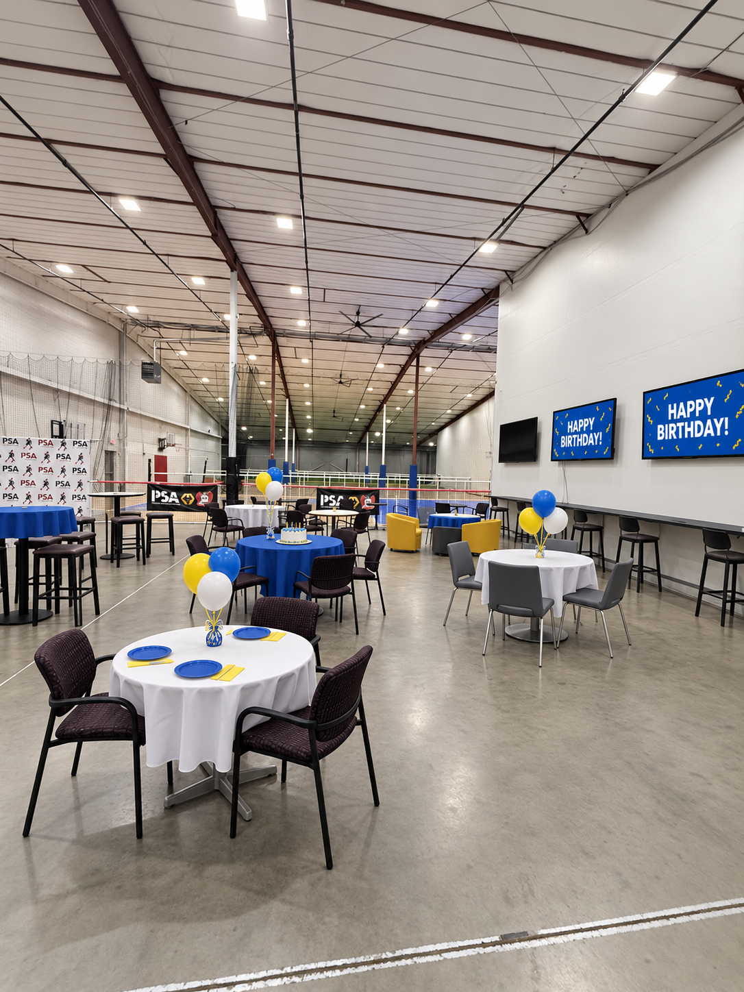 Party and gathering area set with round tables, blue and white linens, balloon centerpieces and Happy Birthday screens, ready for an event