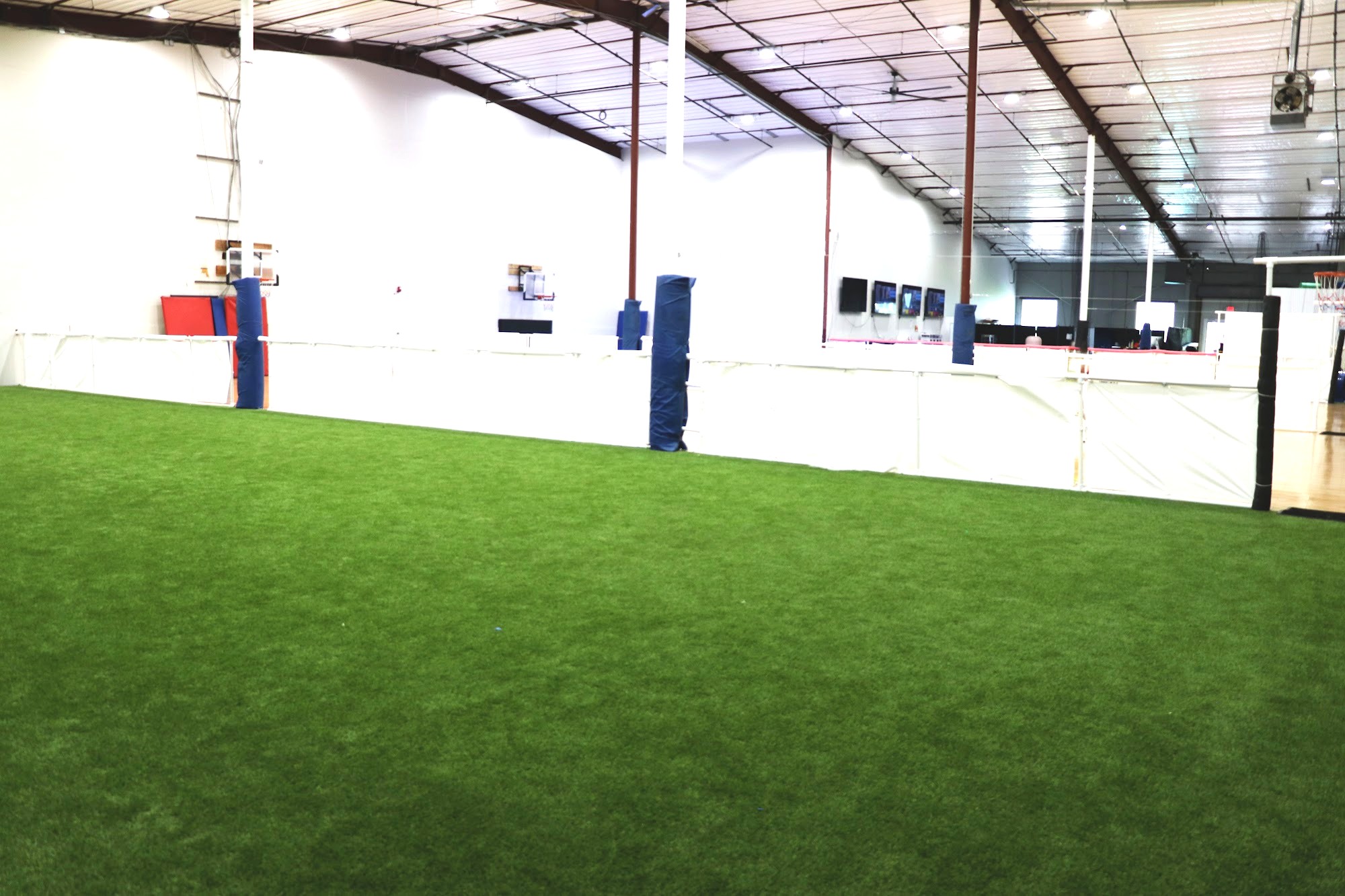 Side view of the indoor turf field meeting the hard court at PSA Sports Club, with blue wall padding and white perimeter boards